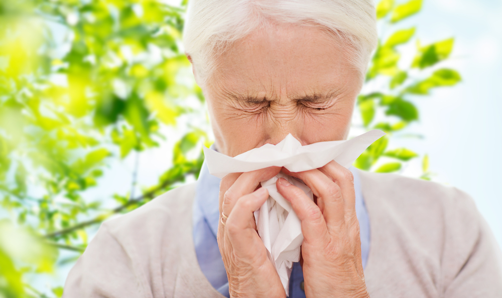 Elderly man blowing nose into a tissue while outdoors