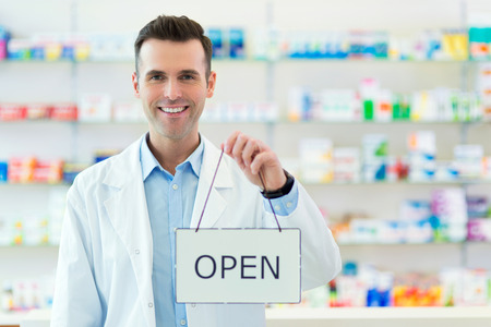 Doctor holding an open sign with blurred shelves in the background